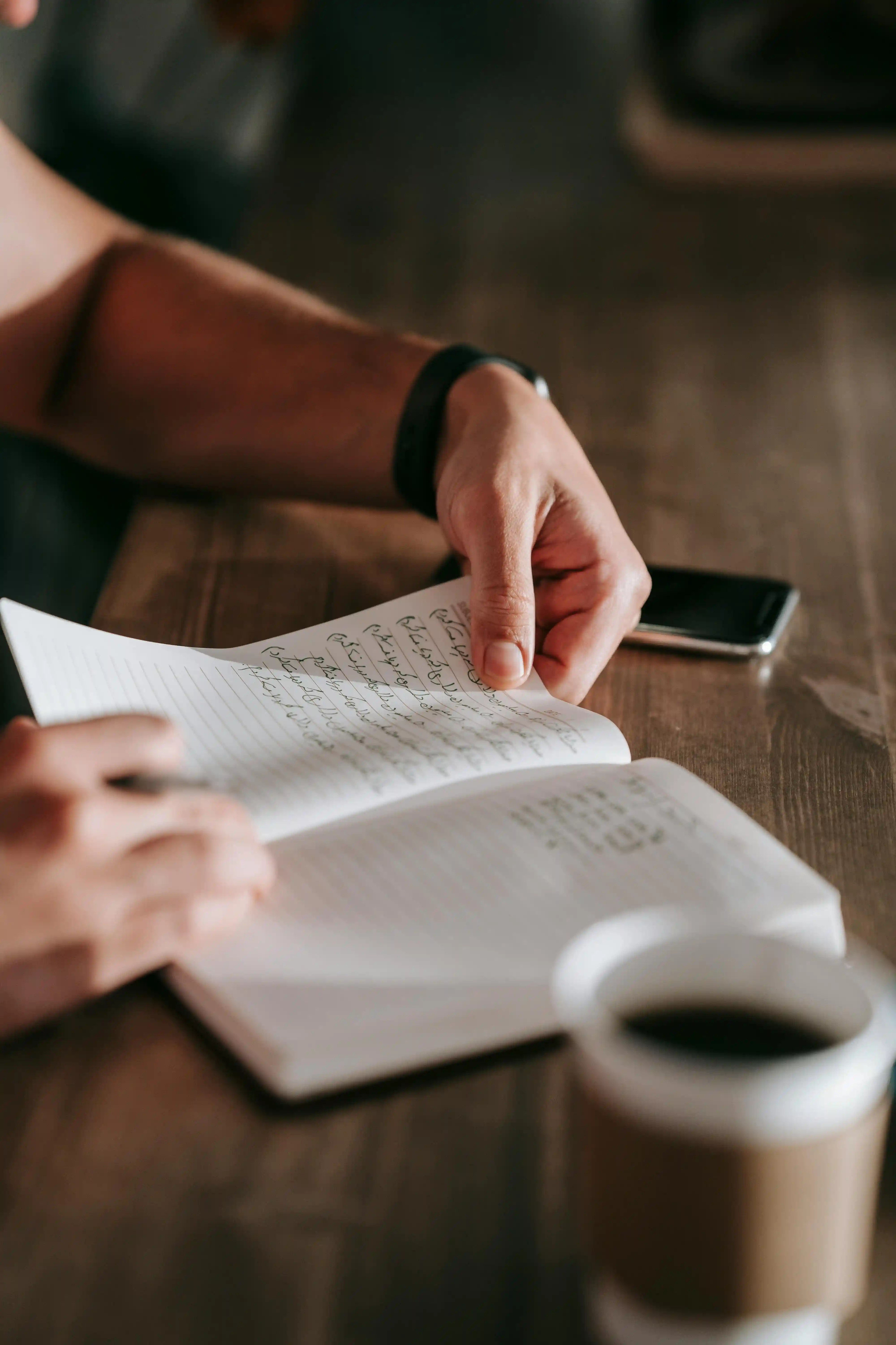 Cuaderno con notas manuscritas junto a café y teléfono — sección de preguntas frecuentes.